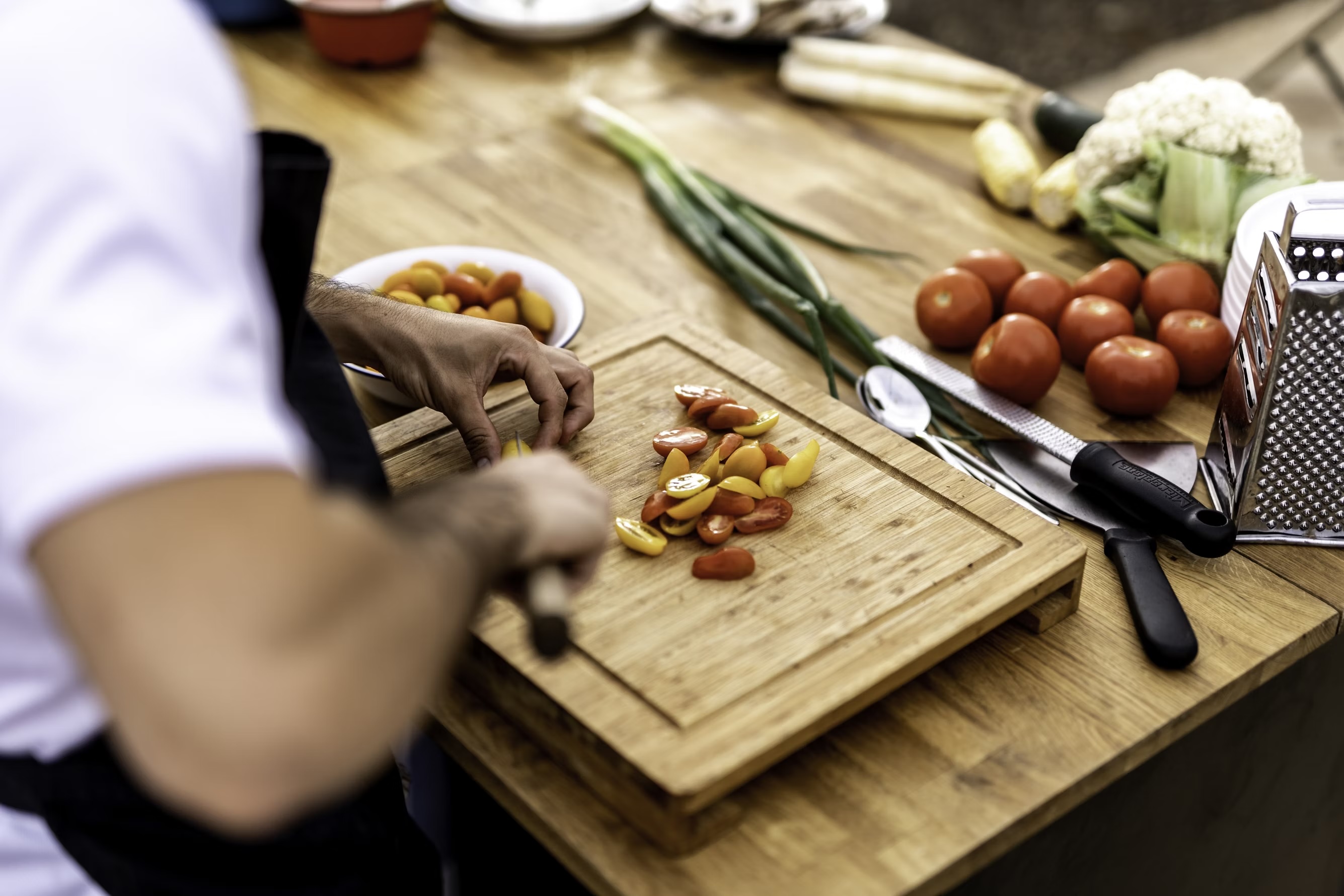 Chef preparing fresh ingredients on a wooden cutting board with tomatoes and vegetables